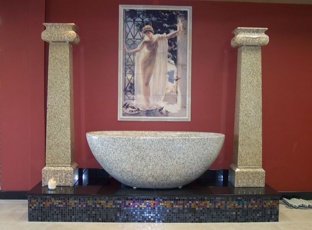 Decorative stone sink with mosaic base and two columns against a red wall, topped by a framed artwork