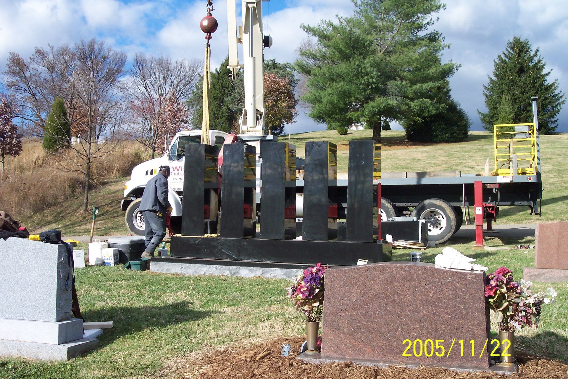 Person loading a black truck beside a gravestone in a cemetery on a sunny day