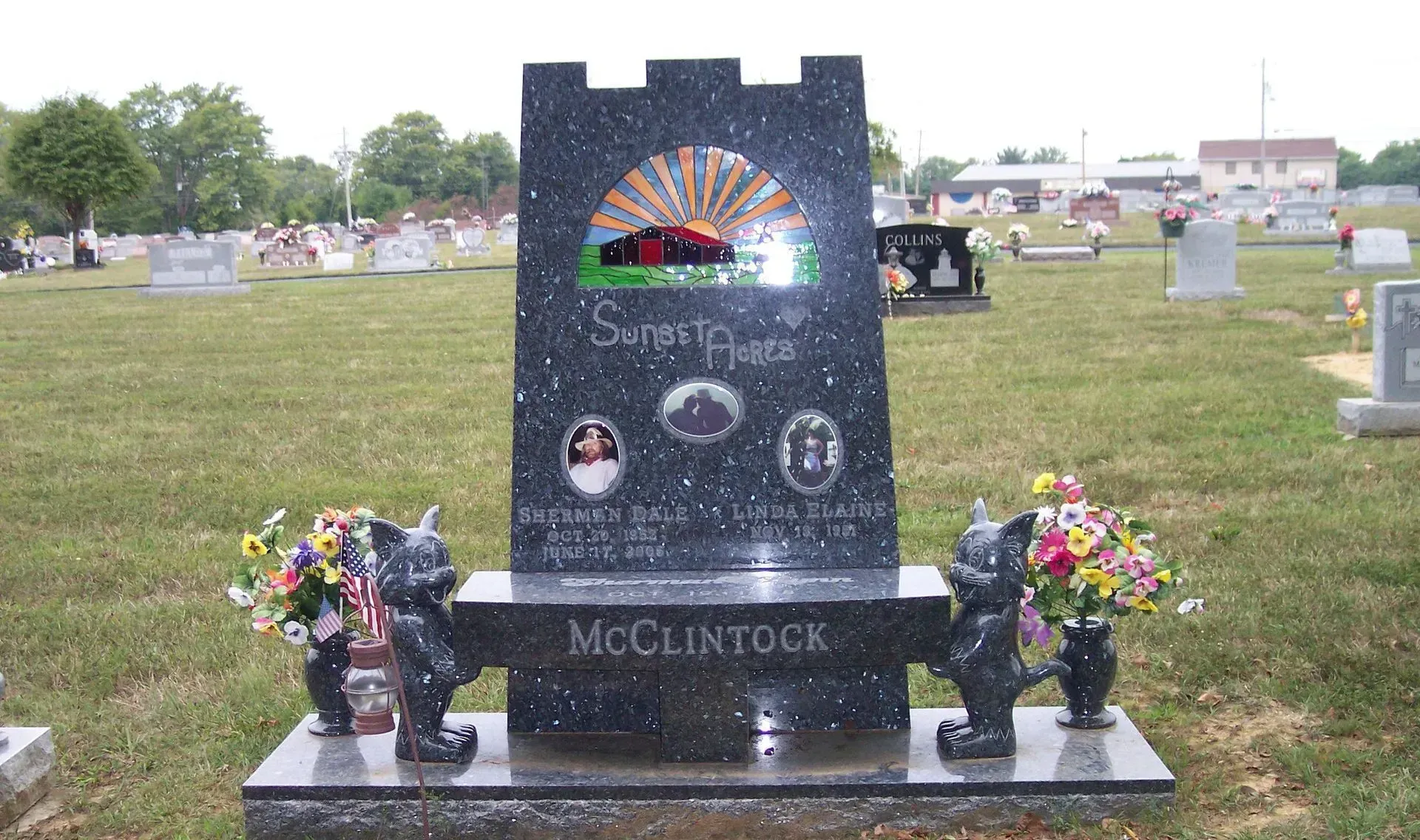 Black granite gravestone with colorful sunset design and flowers in a cemetery