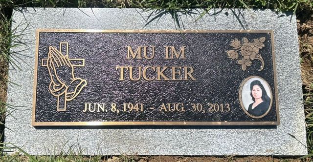 Black granite memorial plaque for Mu Im Tucker with flowers, portrait, and dates Jun. 8, 1941–Aug. 30, 2013.