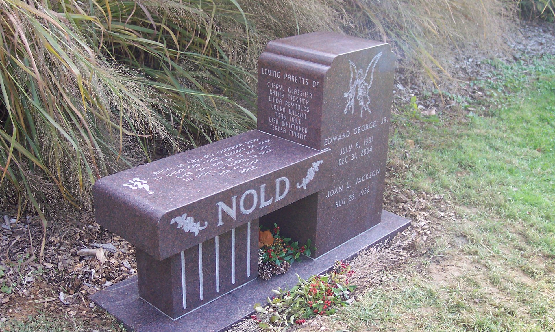 Small brown memorial bench with engraved text beside grassy roadside