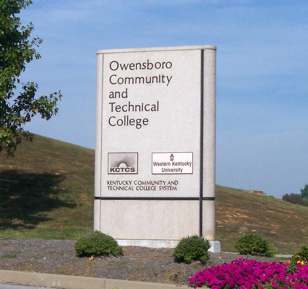 Owensboro Community and Technical College sign beside a grassy hillside and blue sky