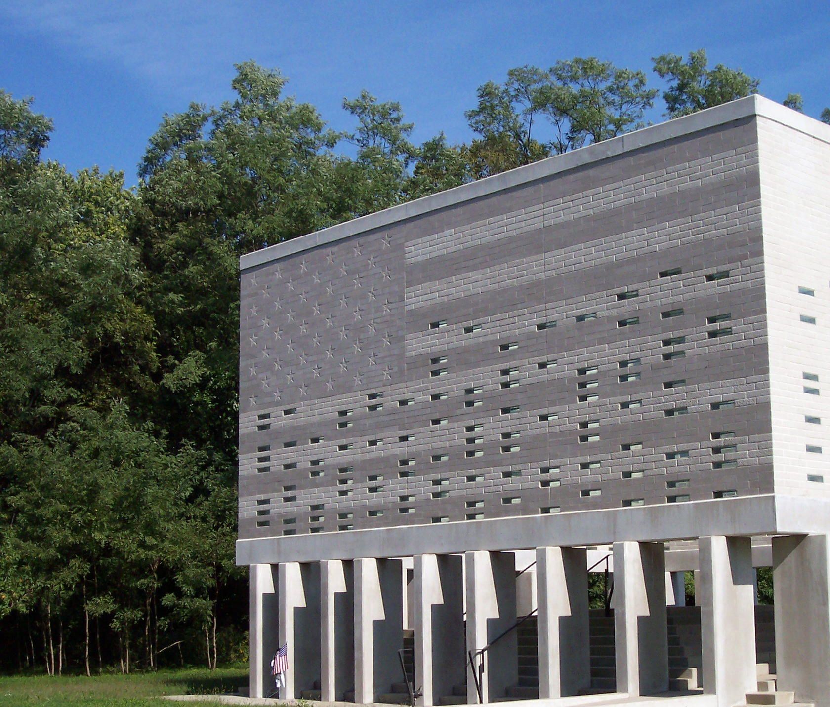 Modern white building with patterned facade and columns, set against trees and blue sky