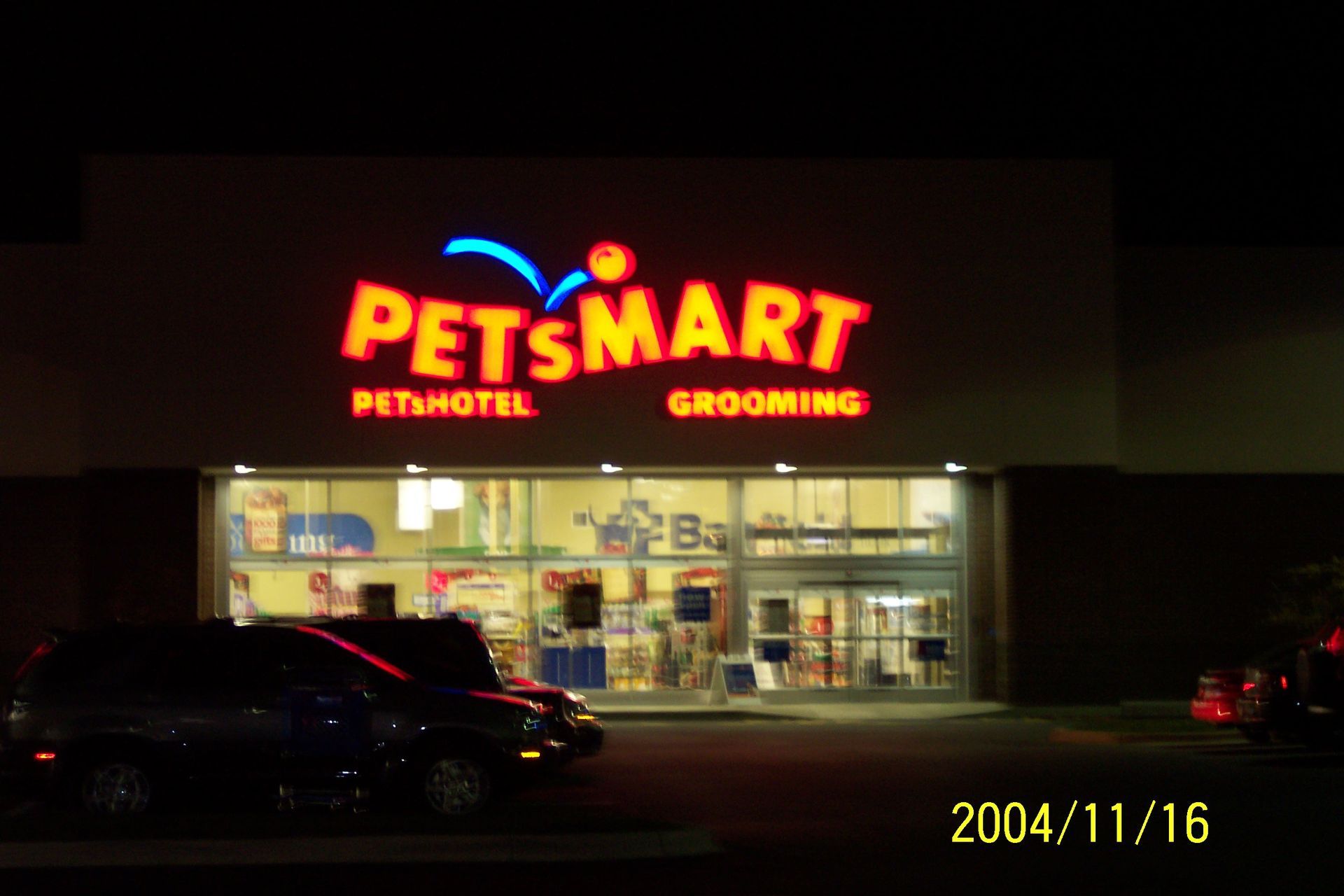 PetSmart storefront at night with bright red sign and parked cars in front