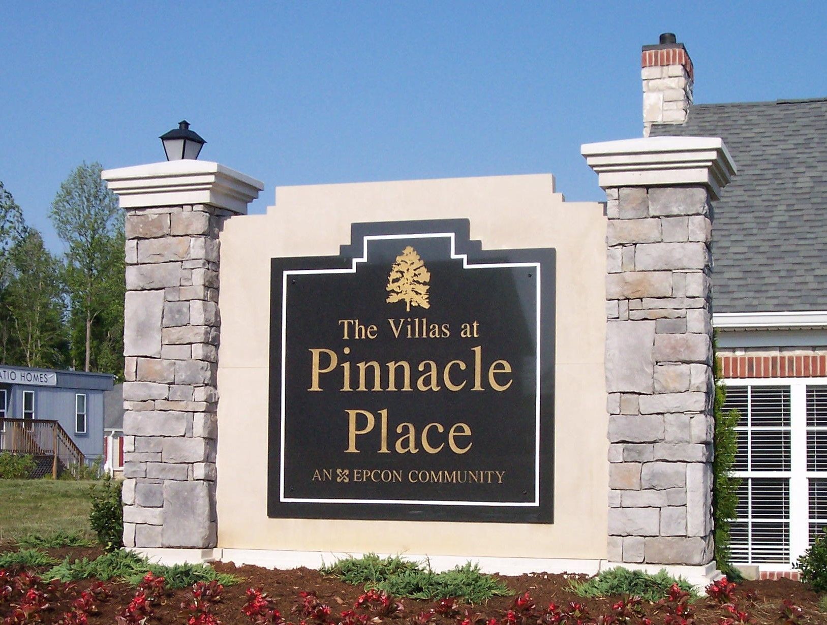 Stone entrance sign for The Villas at Pinnacle Place against a blue sky and landscaped grounds
