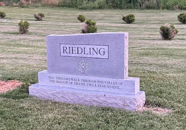 Gray Riedling gravestone in a cemetery with grass and small shrubs nearby