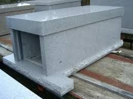 Gray concrete utility box with an open end, sitting on wooden rails outdoors.