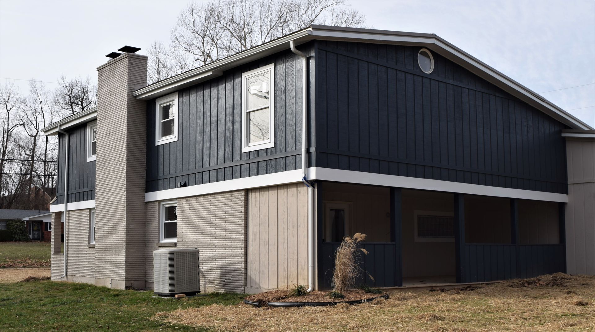 Two-story house with dark siding and light stone exterior, viewed from the front yard.