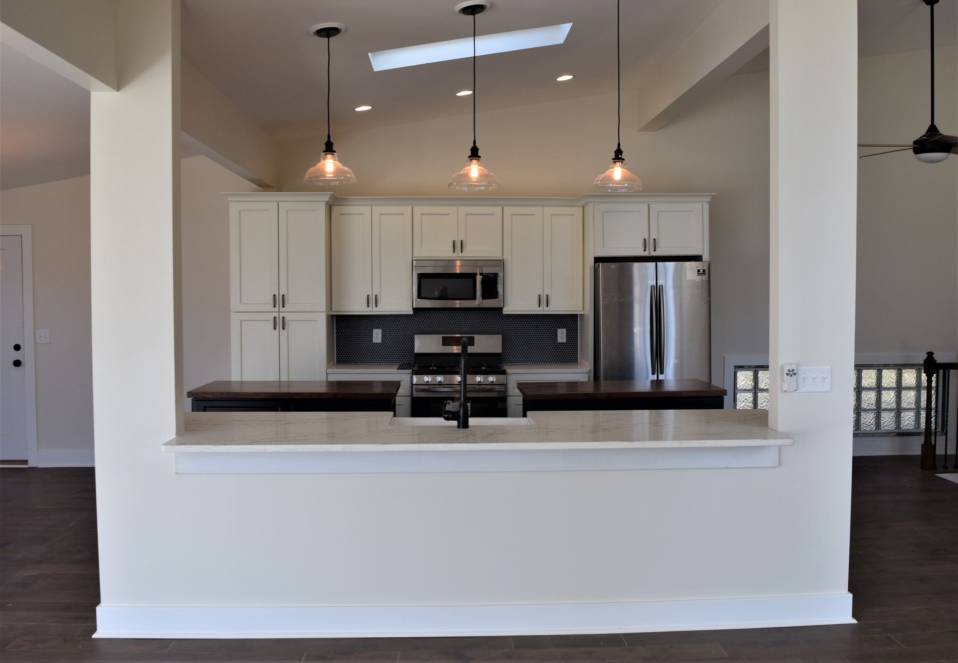 Bright kitchen with white cabinets, stainless steel appliances, dark island counter, and pendant lights