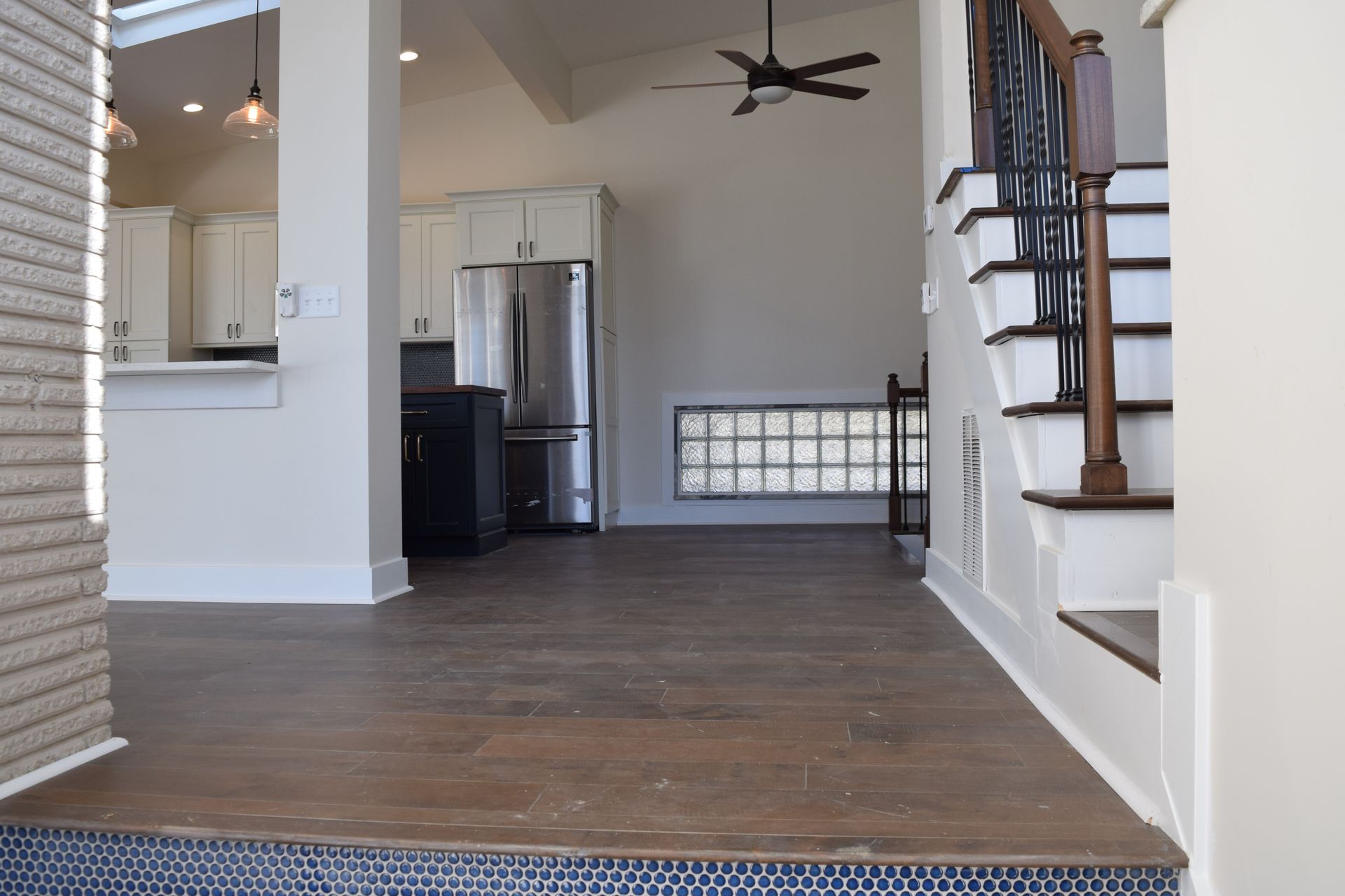 Open living area with hardwood floors, staircase, kitchen, and ceiling fan.