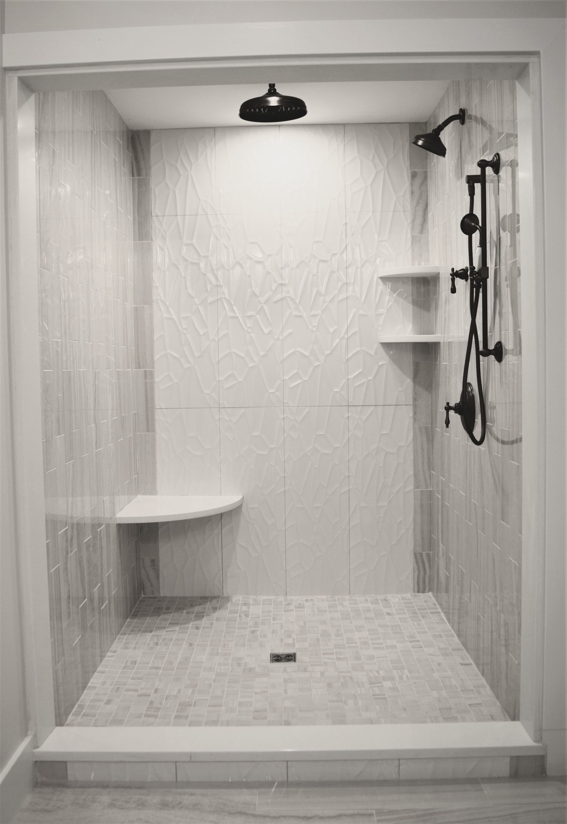 Empty white tiled shower with bench, shelf, and dual shower fixtures.