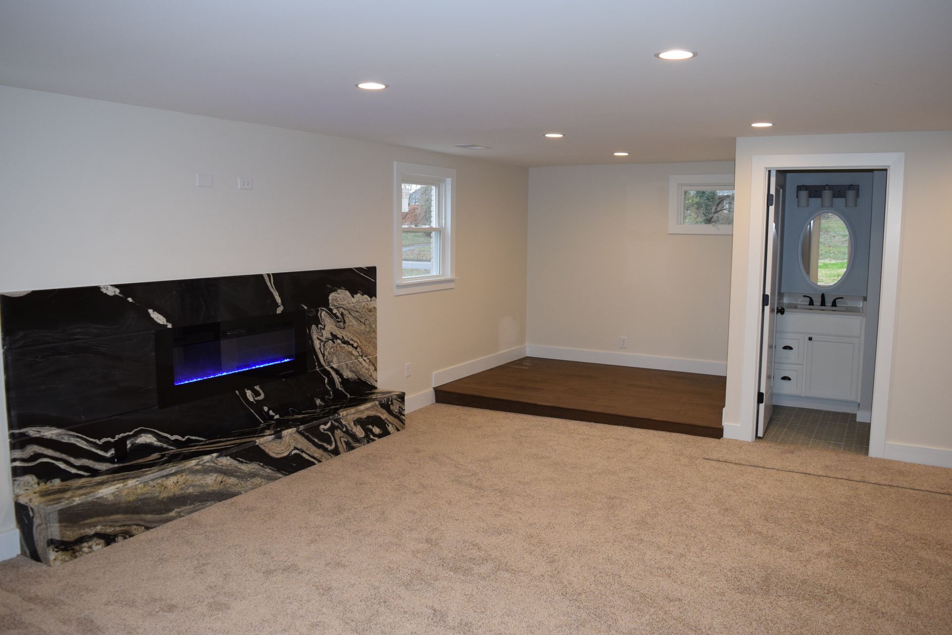 Empty carpeted living room with a black marble fireplace and a small raised entryway.
