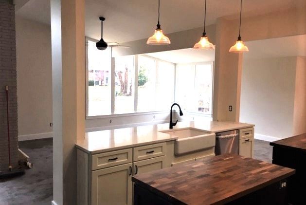 Bright kitchen with large window, white cabinets, pendant lights, and a dark wood island table.