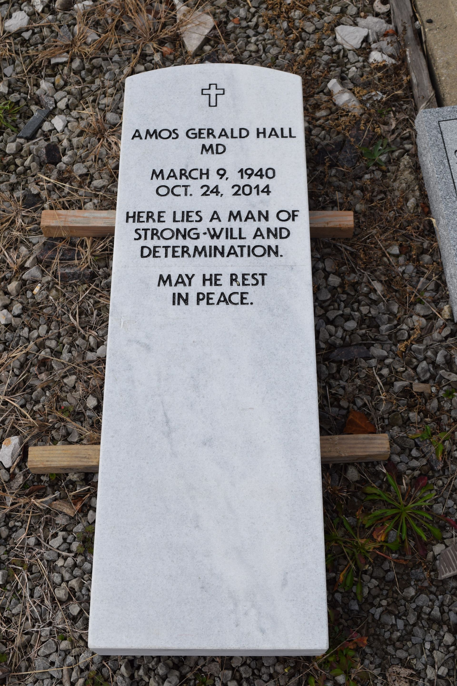 White memorial grave marker with engraved tribute and small cross, set in gravel.