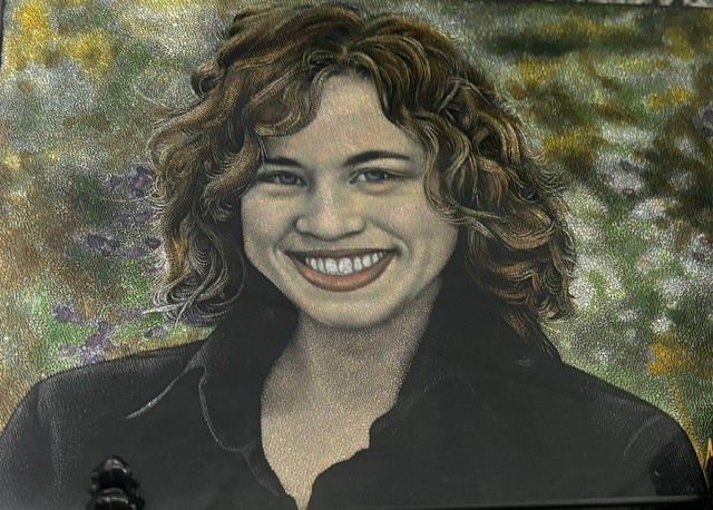 Smiling woman with curly hair in a dark jacket against a softly blurred floral background