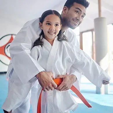 A man is carrying a little girl on his shoulders in a karate class.