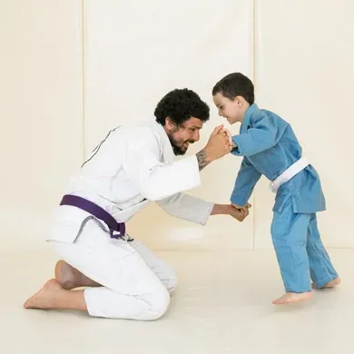 A man in a white karate uniform is kneeling down next to a little boy in a blue karate uniform