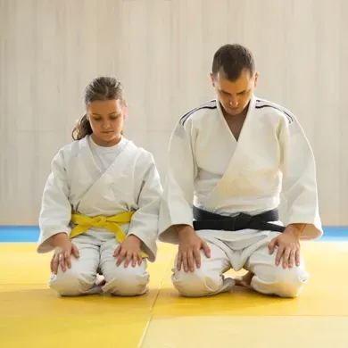 A man and a girl are kneeling on a yellow mat.