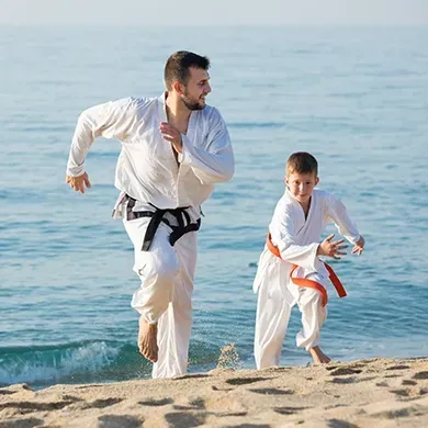 A man and a boy are practicing karate on the beach.