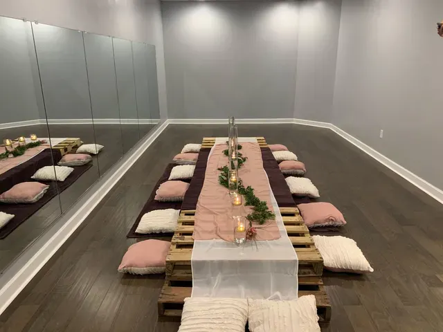 A low, wooden pallet picnic table set for a floor-seated event, decorated with candles, greenery, and cushions in a room.