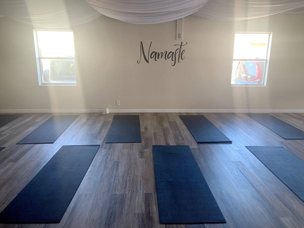 Yoga studio with a Namaste wall decal, wooden floors, and several dark yoga mats arranged for a class.
