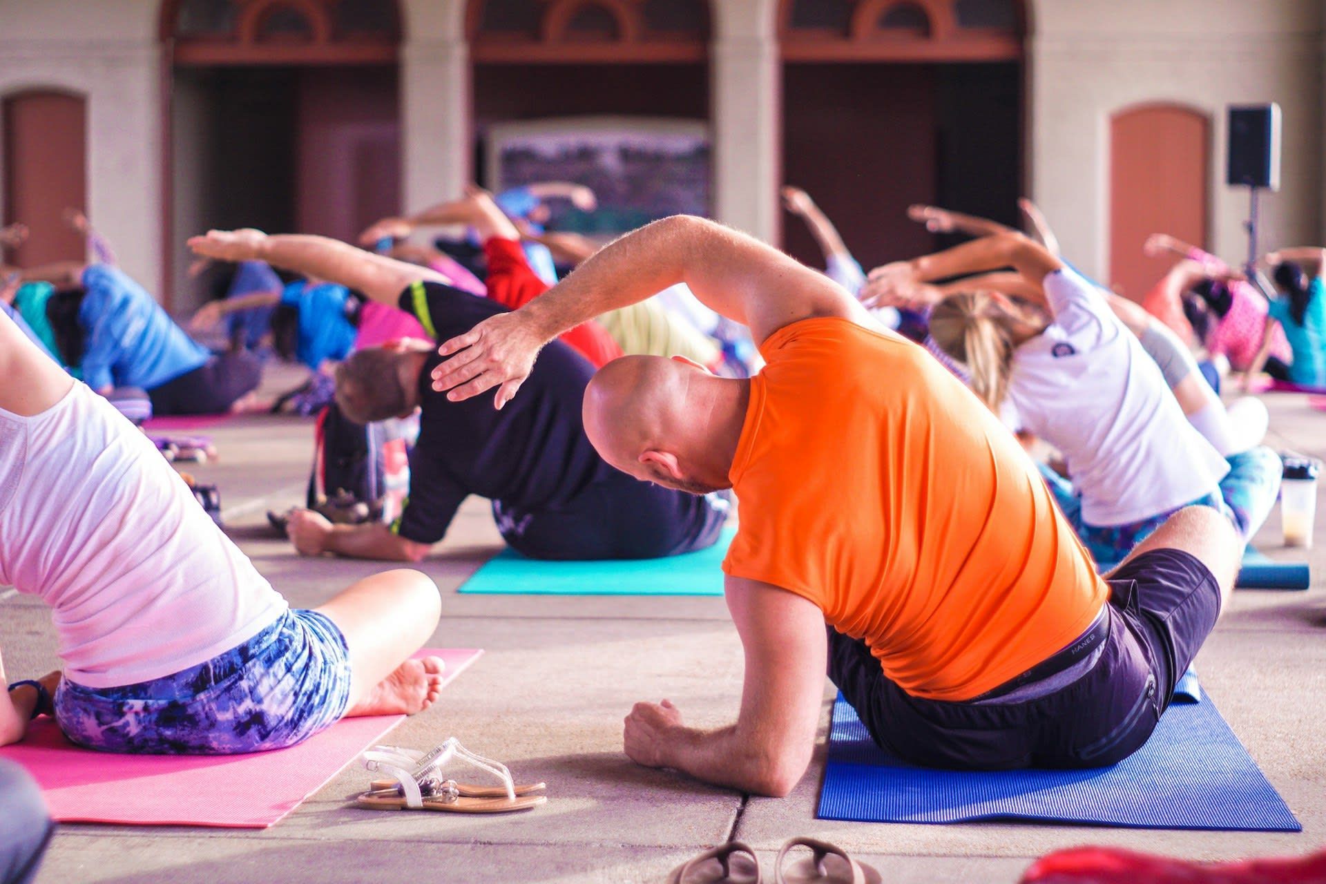 A group of people practicing yoga on colorful mats in an open-air indoor space.