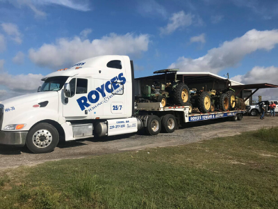 White Royce's semi-truck hauling antique tractors on a trailer under a blue sky.