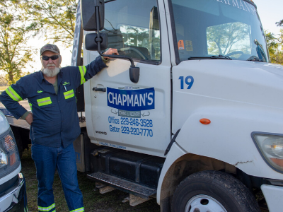 Man standing next to a Chapman's tow truck in an outdoor setting.