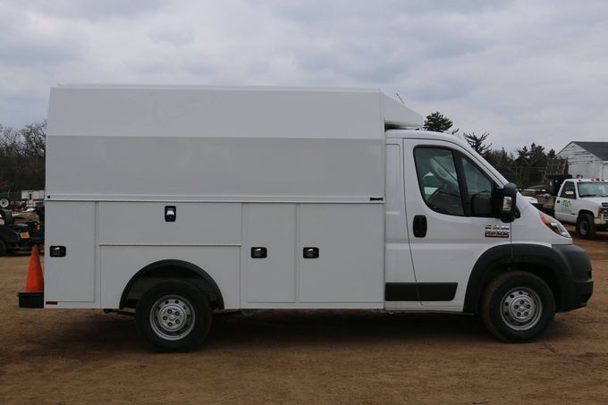 White utility truck parked on dirt. Side view showing storage compartments and elevated roof.