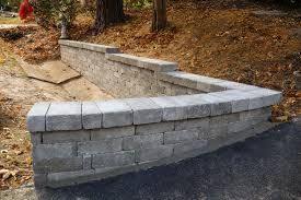 Curved gray block retaining wall along a sloped dirt path beside a paved road