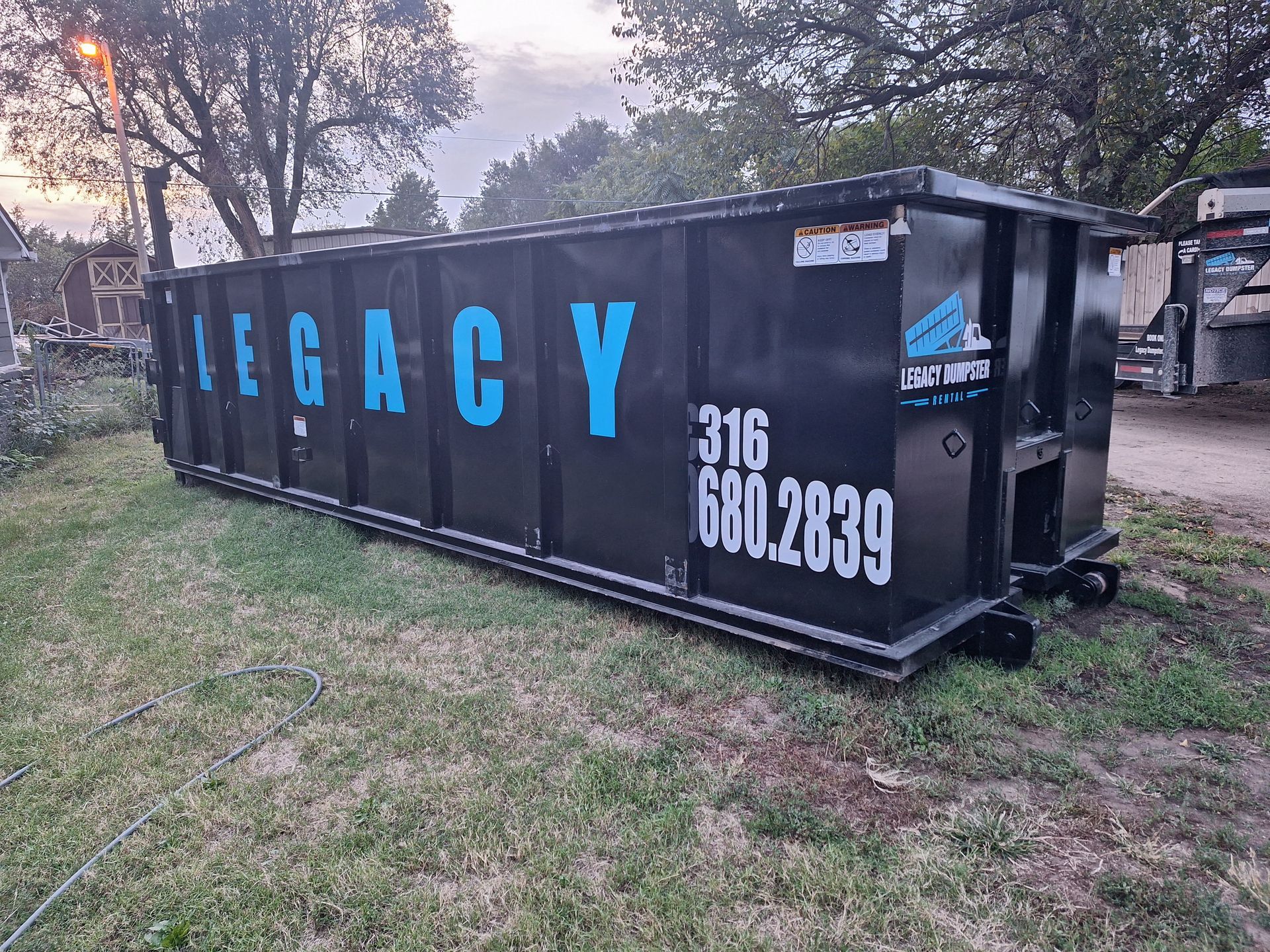 A large black dumpster is sitting on top of a lush green field.