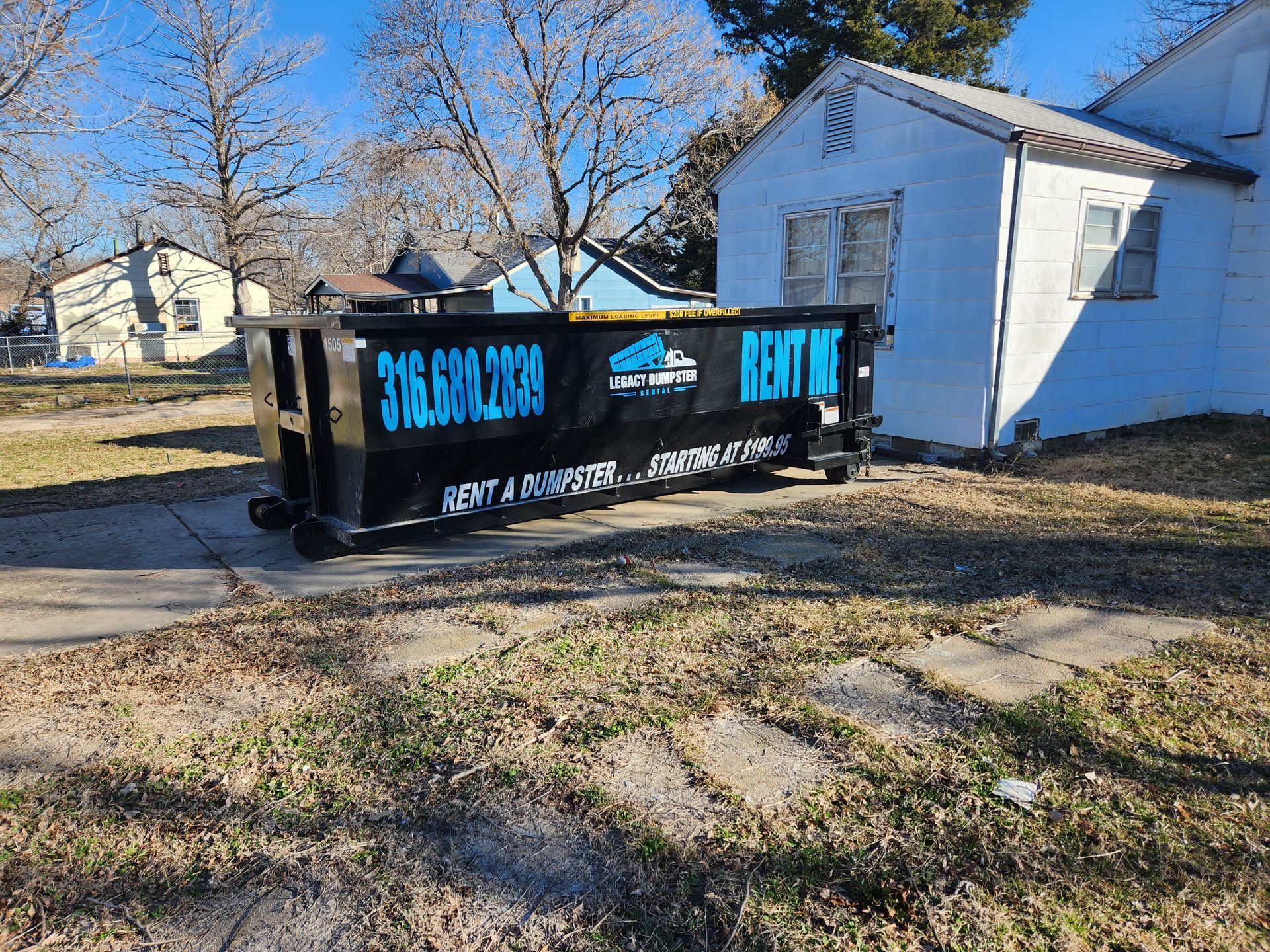 A dumpster is parked in front of a white house.