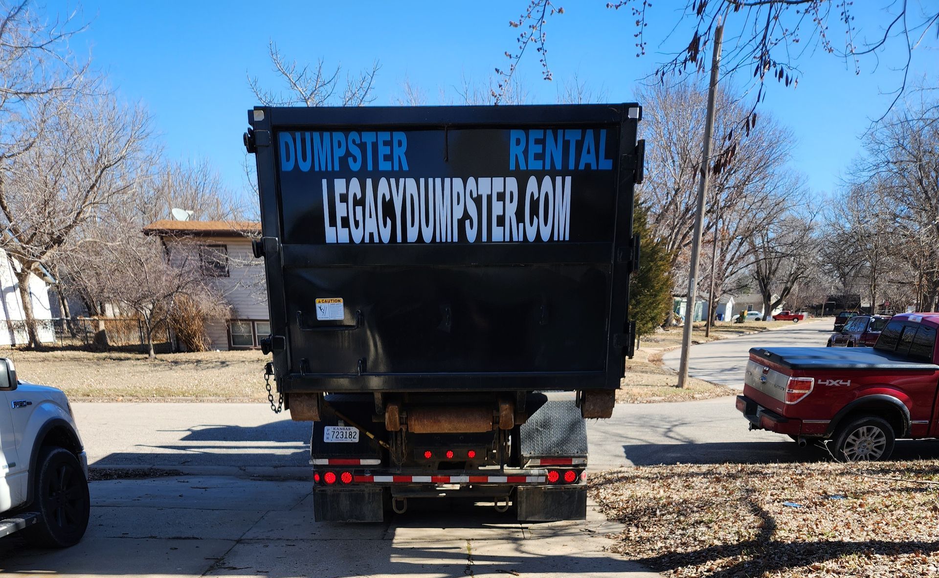 A dumpster with the website legacydumpster.com on the back is parked in a parking lot.