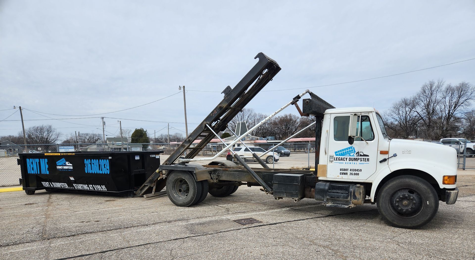 A dump truck is pulling a dumpster in a parking lot.