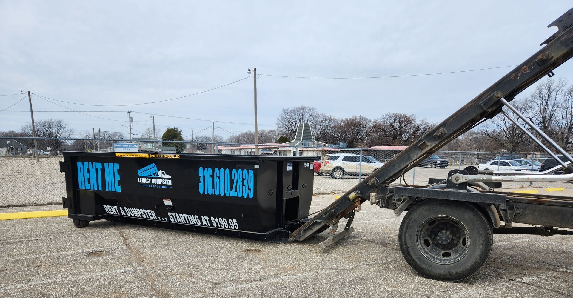A dumpster is being towed by a truck in a gravel lot.