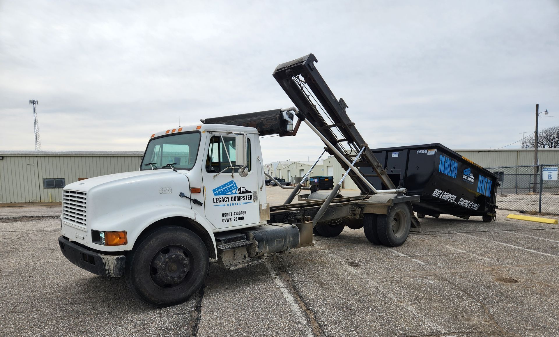A dump truck with a dumpster attached to it is parked in a gravel lot.