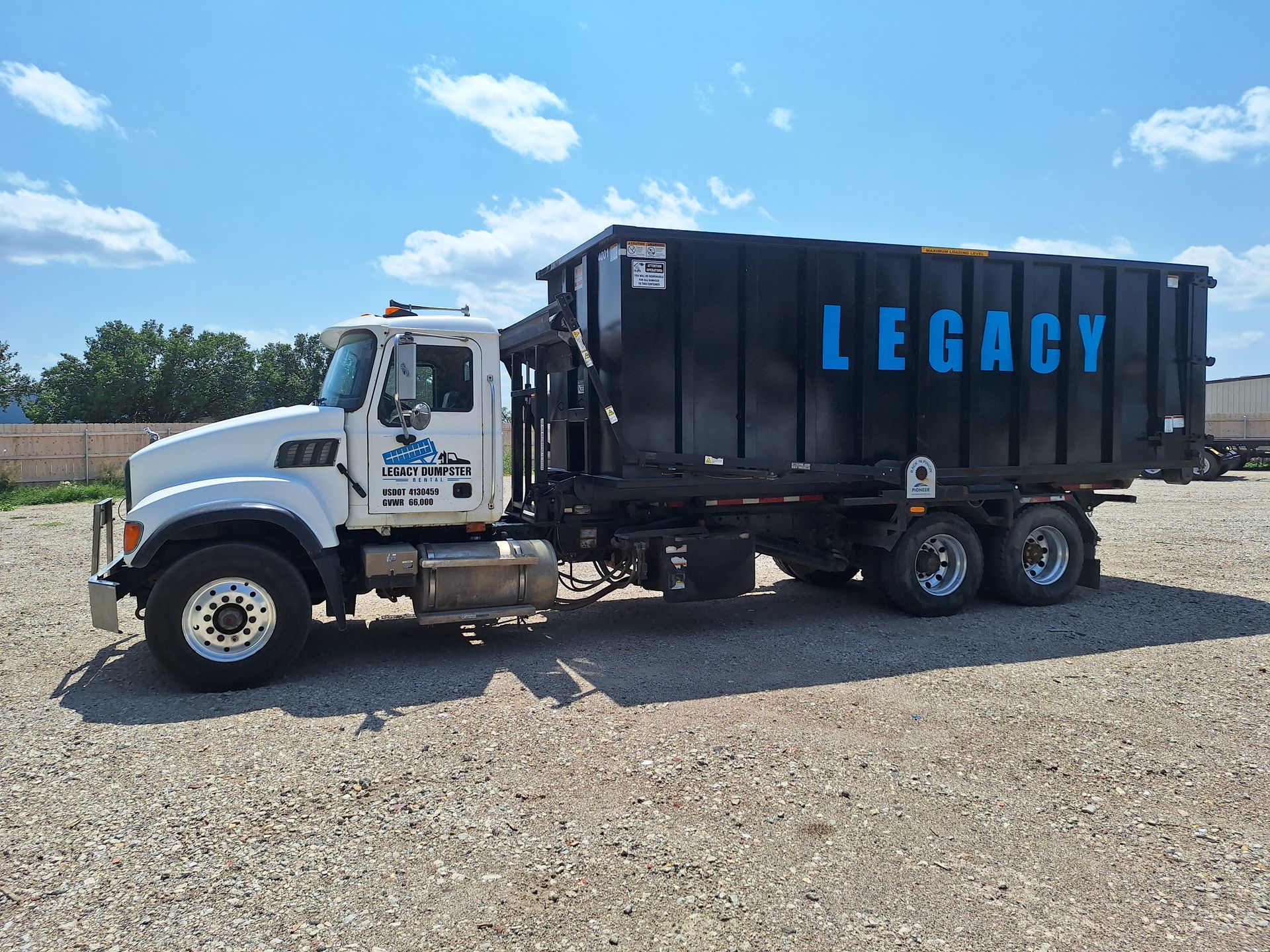 A dump truck with the word legacy on the side is parked in a gravel lot.