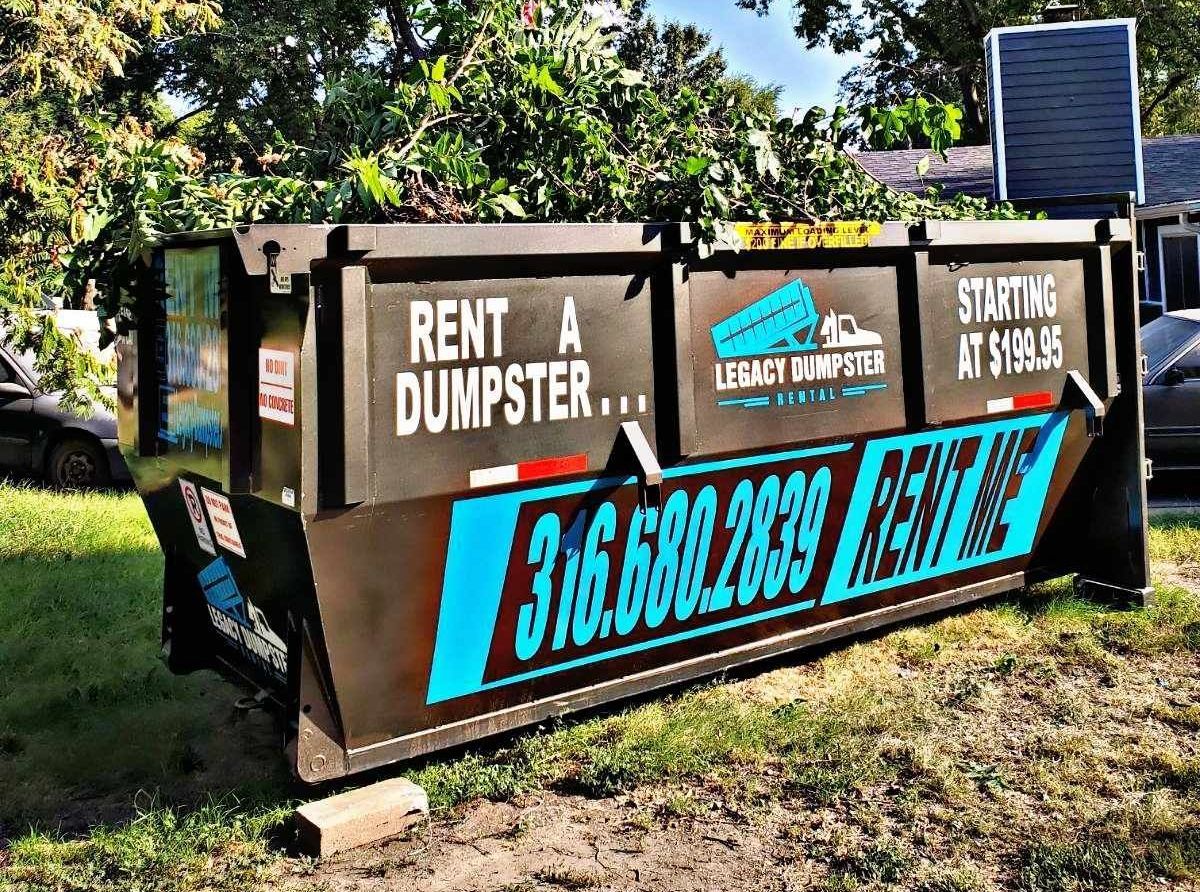 A large dumpster is sitting in the grass in front of a house.