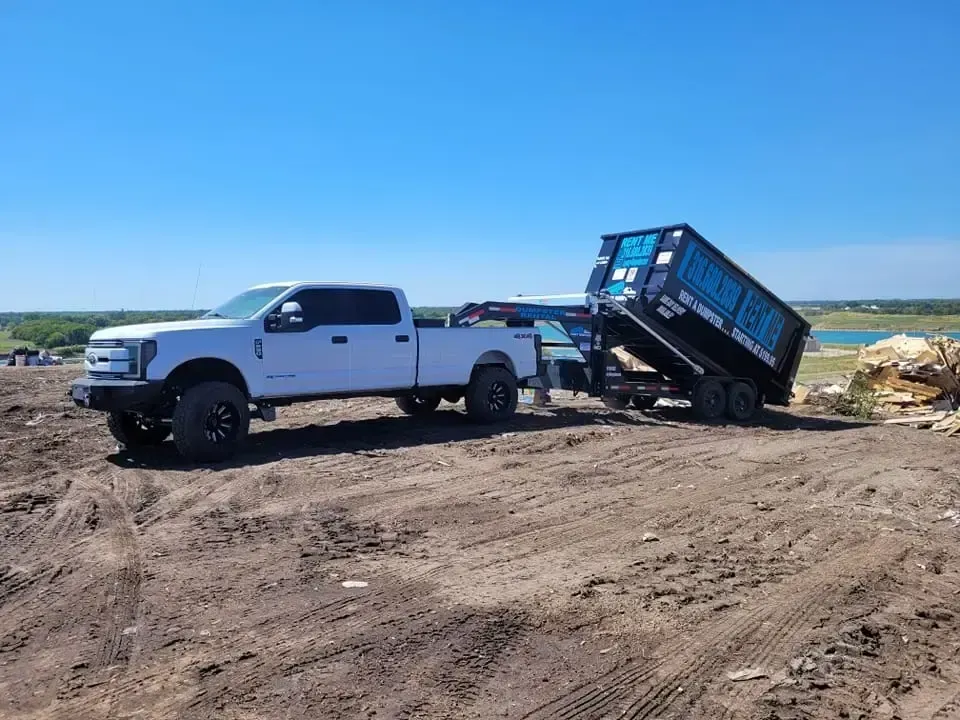 A dump truck is dropping off a 20 yard dumpster in the grass in Wellington