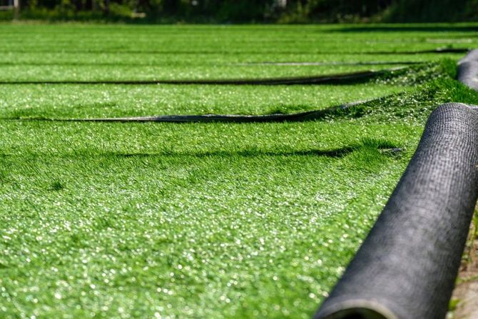 Artificial turf field with a rolled-up edge and lines, green grass, bright sunlight.