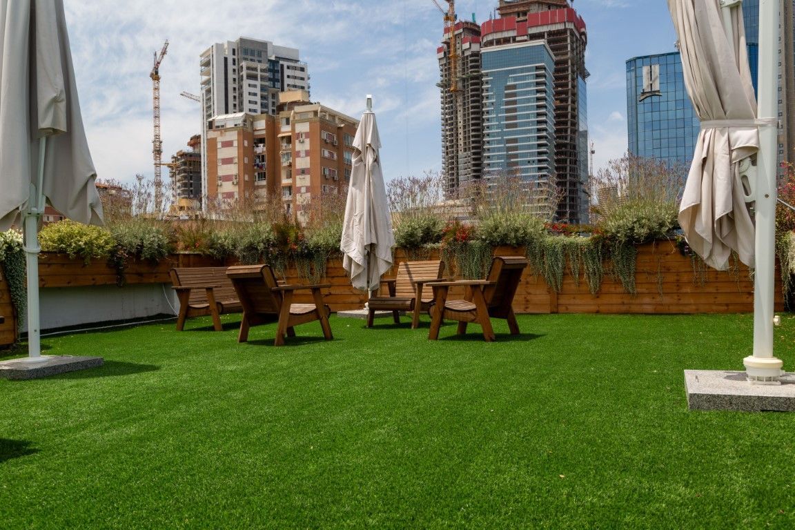Rooftop patio with green turf, wooden chairs and tables, and city skyline view.