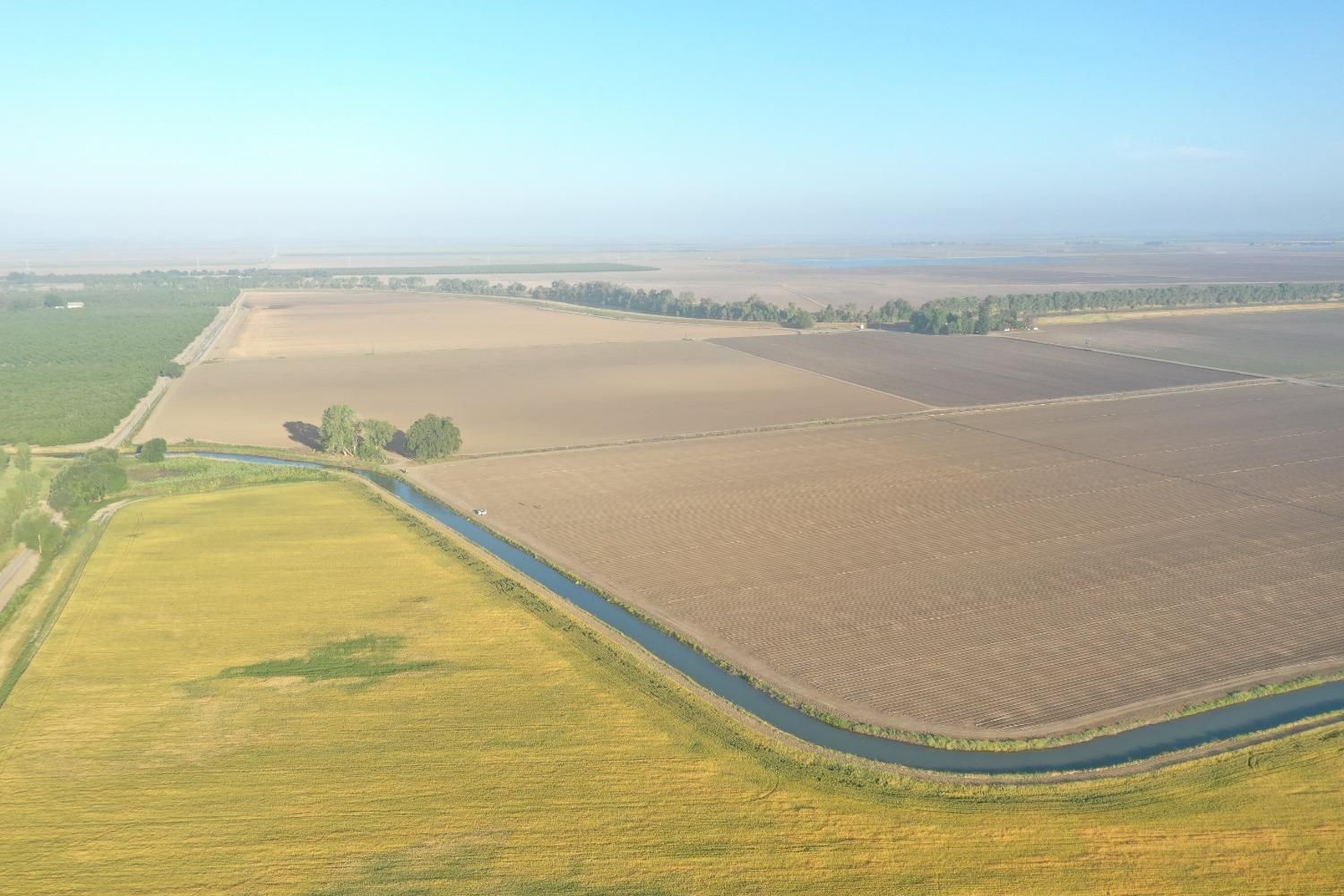 Aerial view of farmland with irrigation canal, varied colors of fields, clear sky.