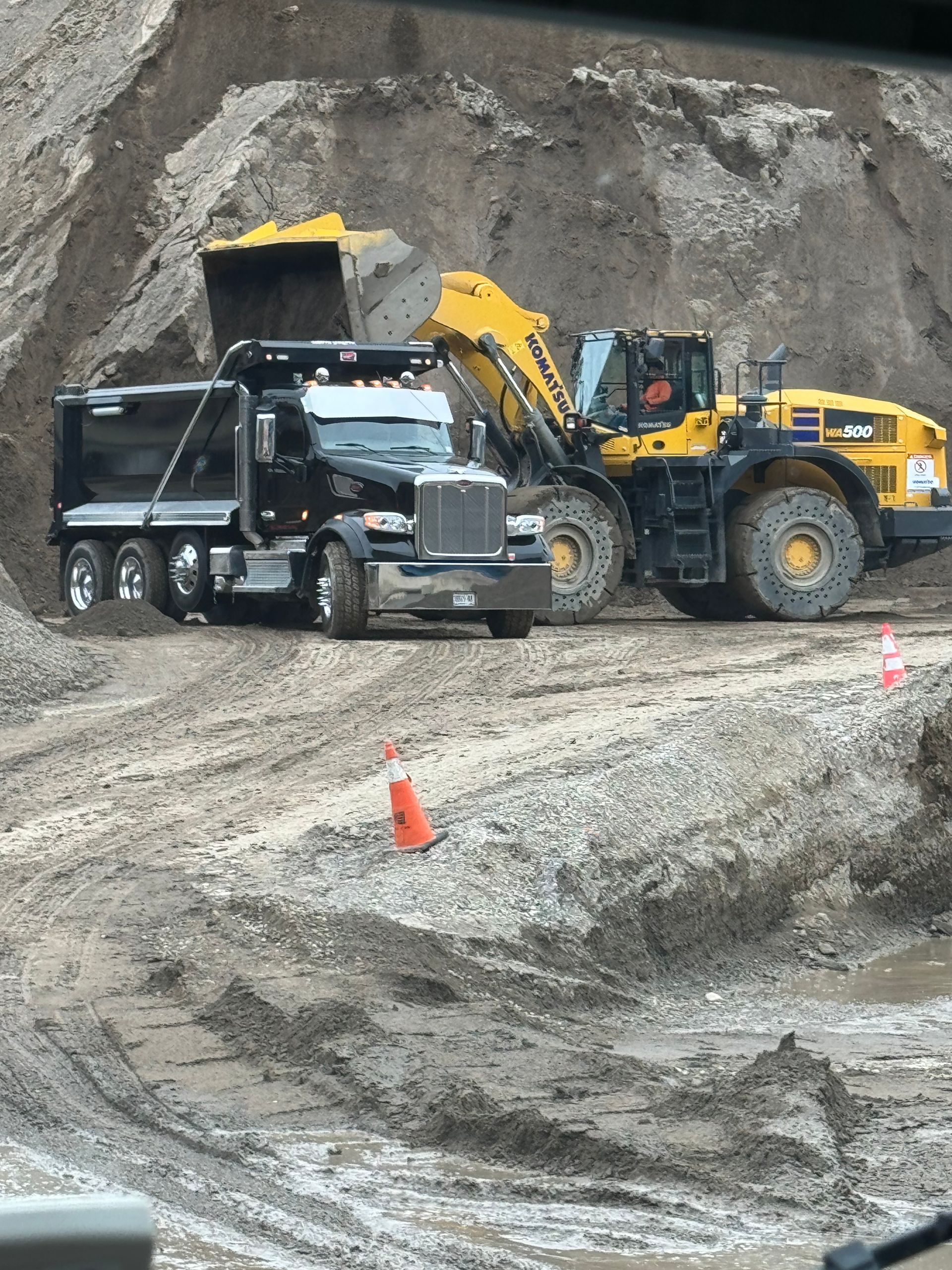 A dump truck is being loaded with dirt by a yellow bulldozer