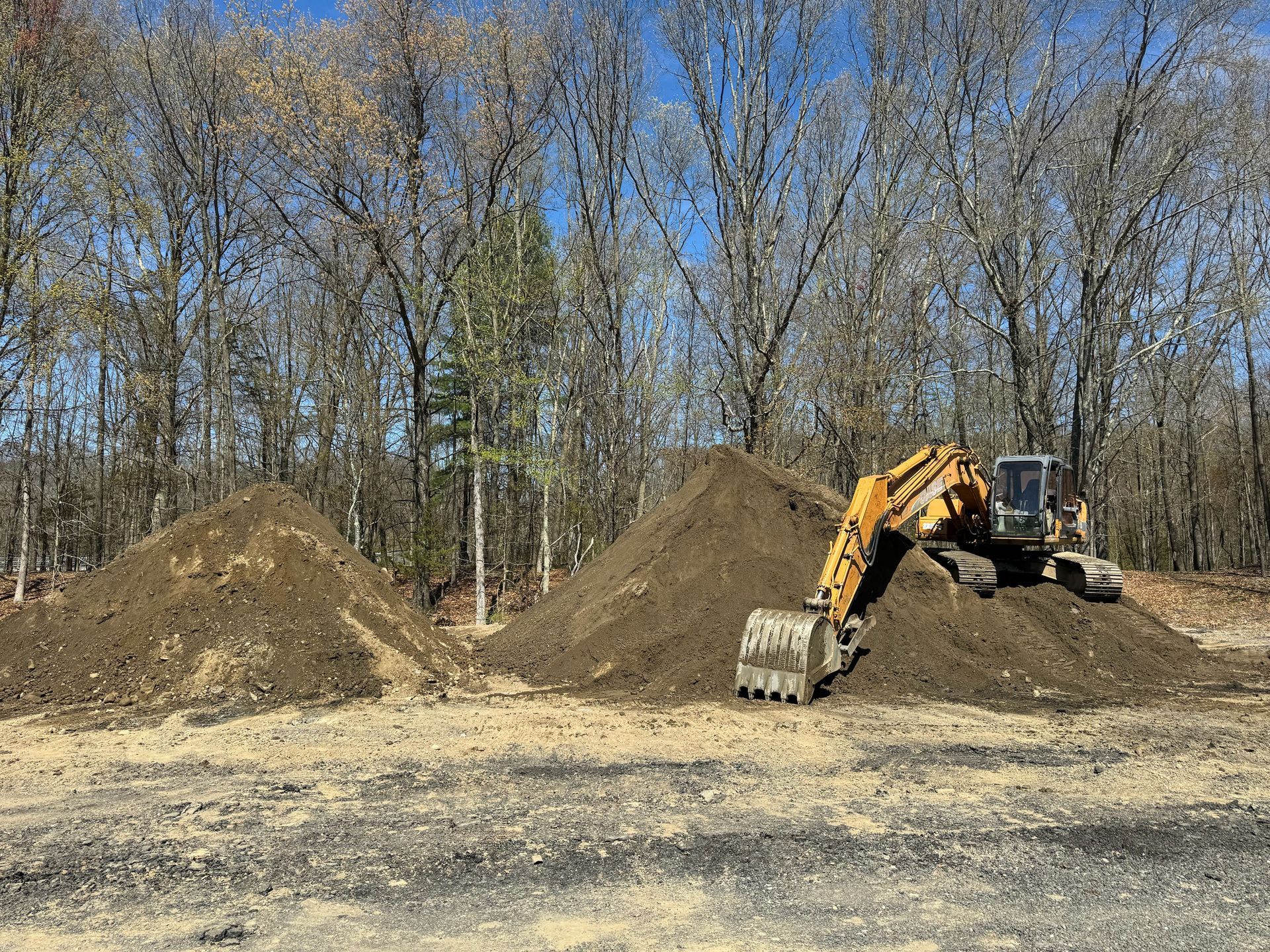 A yellow excavator is working on a pile of dirt in a field.