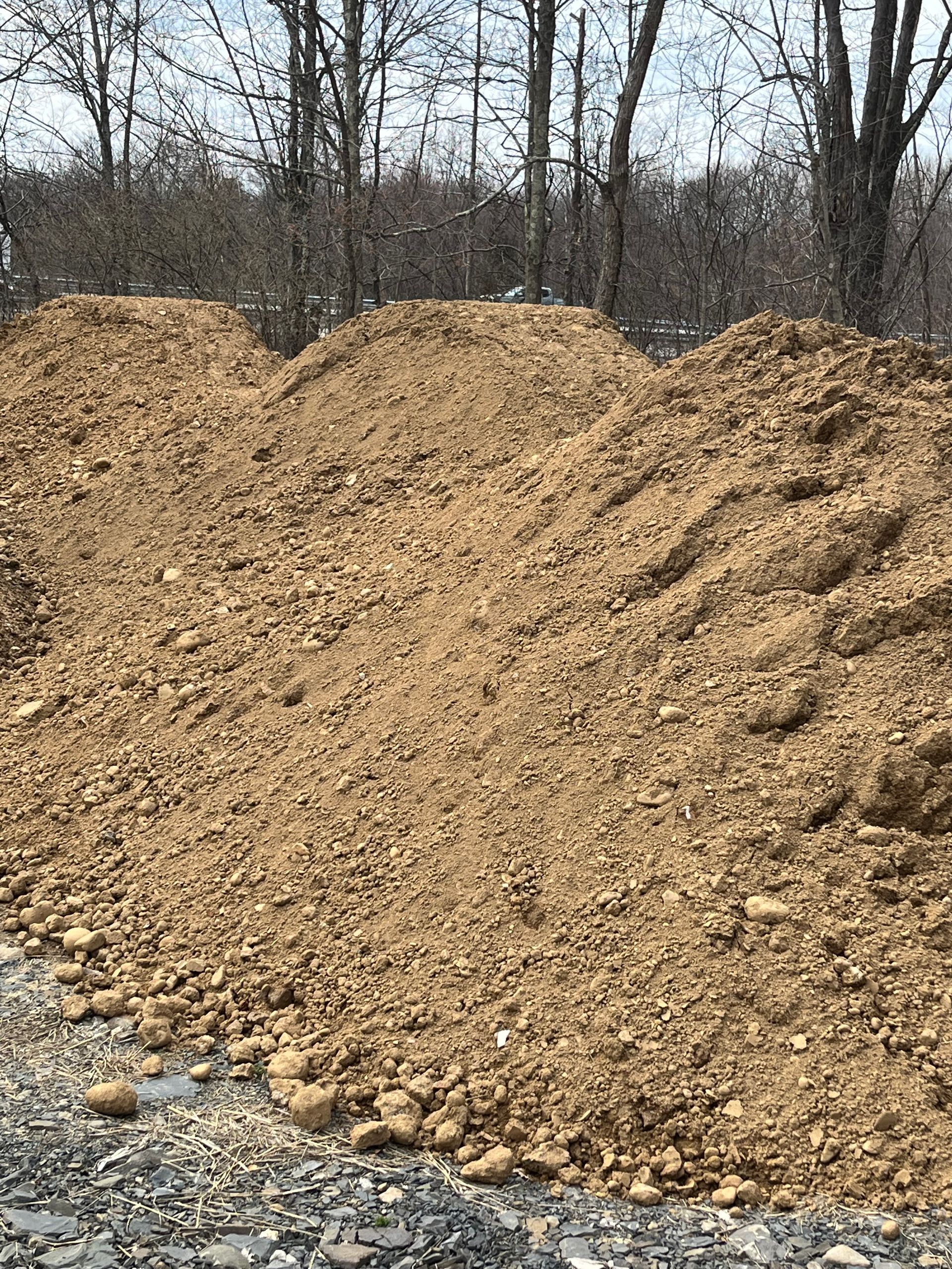 A pile of dirt is sitting on the side of a road next to a forest.