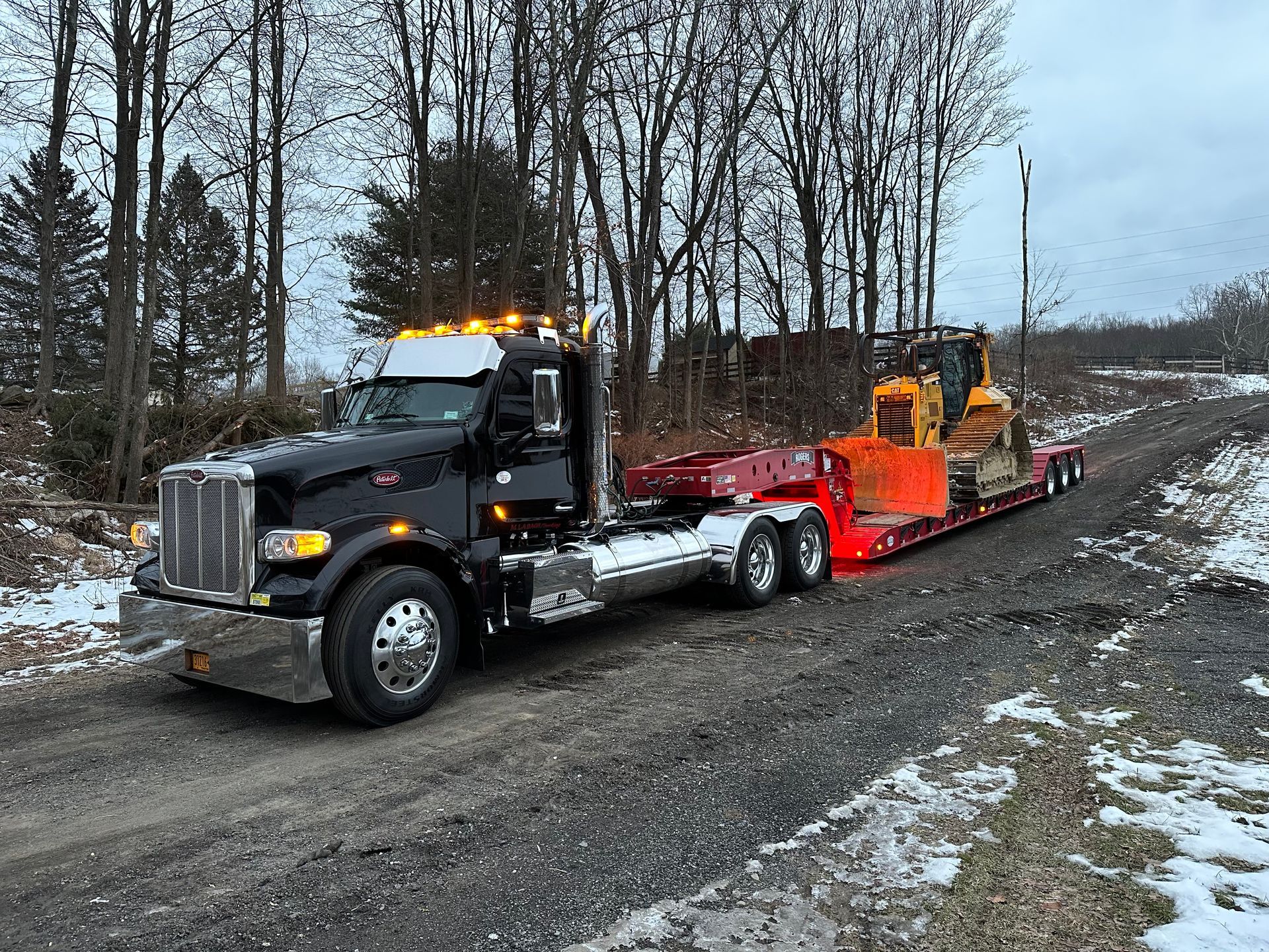 A semi truck is carrying a bulldozer down a snowy road.