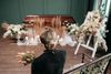 Woman in black holding flowers, facing a casket and floral arrangements at a funeral.