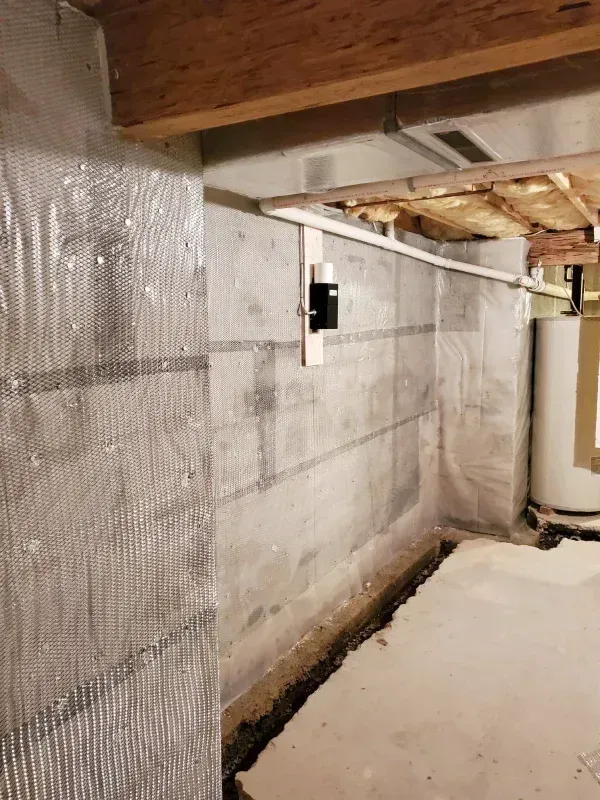 Concrete basement wall with reflective insulation, structural repairs, and a white water heater in the corner.