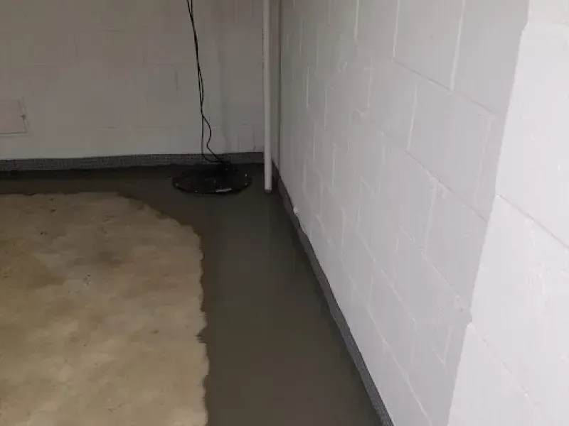 A dark pool of water on a concrete floor along a white painted cinder block wall in a basement.