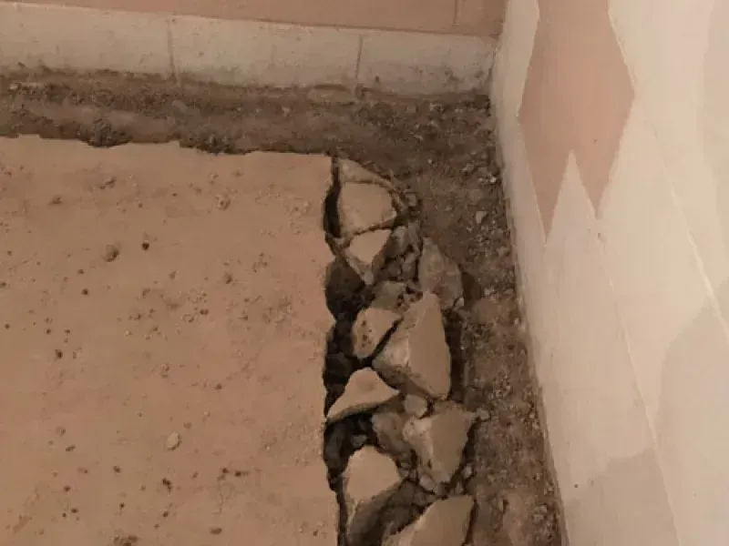 A section of concrete floor has been broken away along a corner wall, exposing loose gravel and rubble beneath.